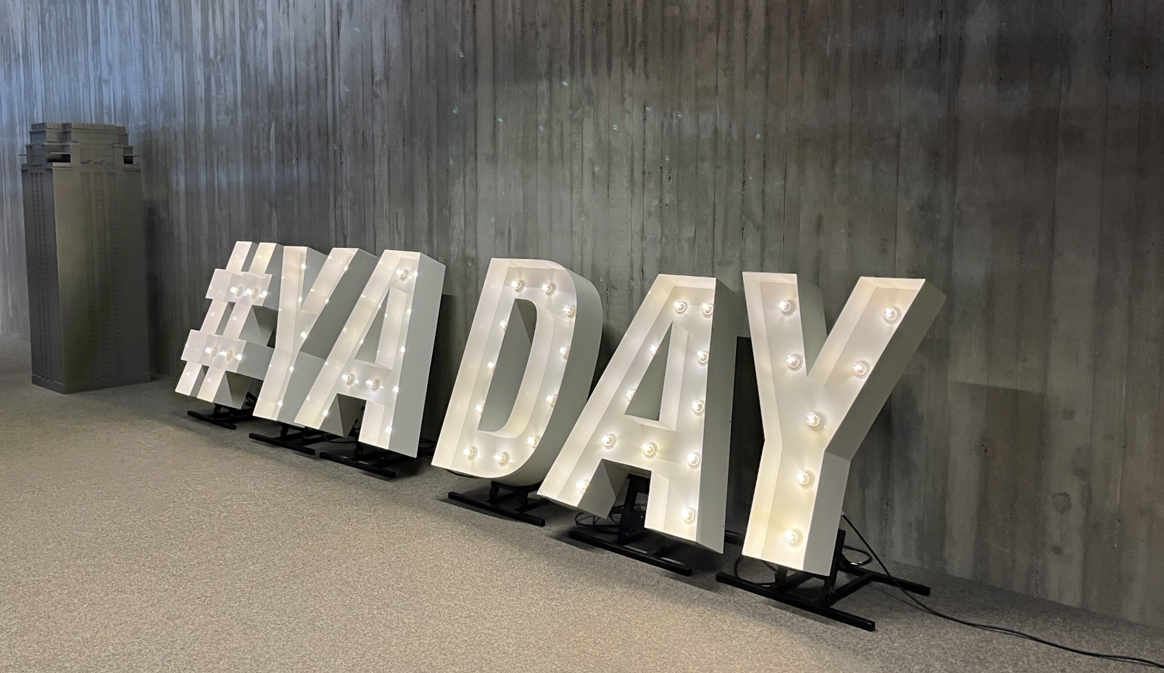 grote letter YA DAY met daarin brandende lampen staan gekanteld tegen een muur