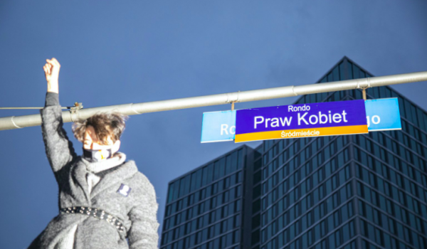 Een vrouw staat met geheven vuist naast een plakkaat getiteld Rondo Praw Kobiet
